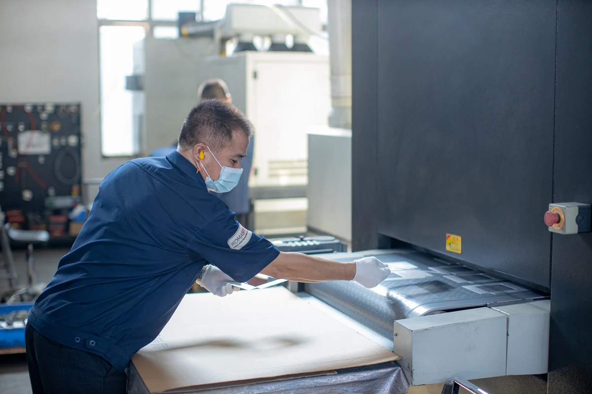 Boda technician wearing gloves and a mask deburring a stainless steel part on an in-line finishing machine