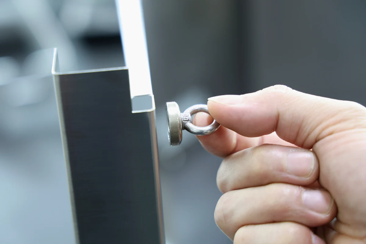 Pot magnet held against the formed flange of a brushed 316 stainless steel sheet metal panel