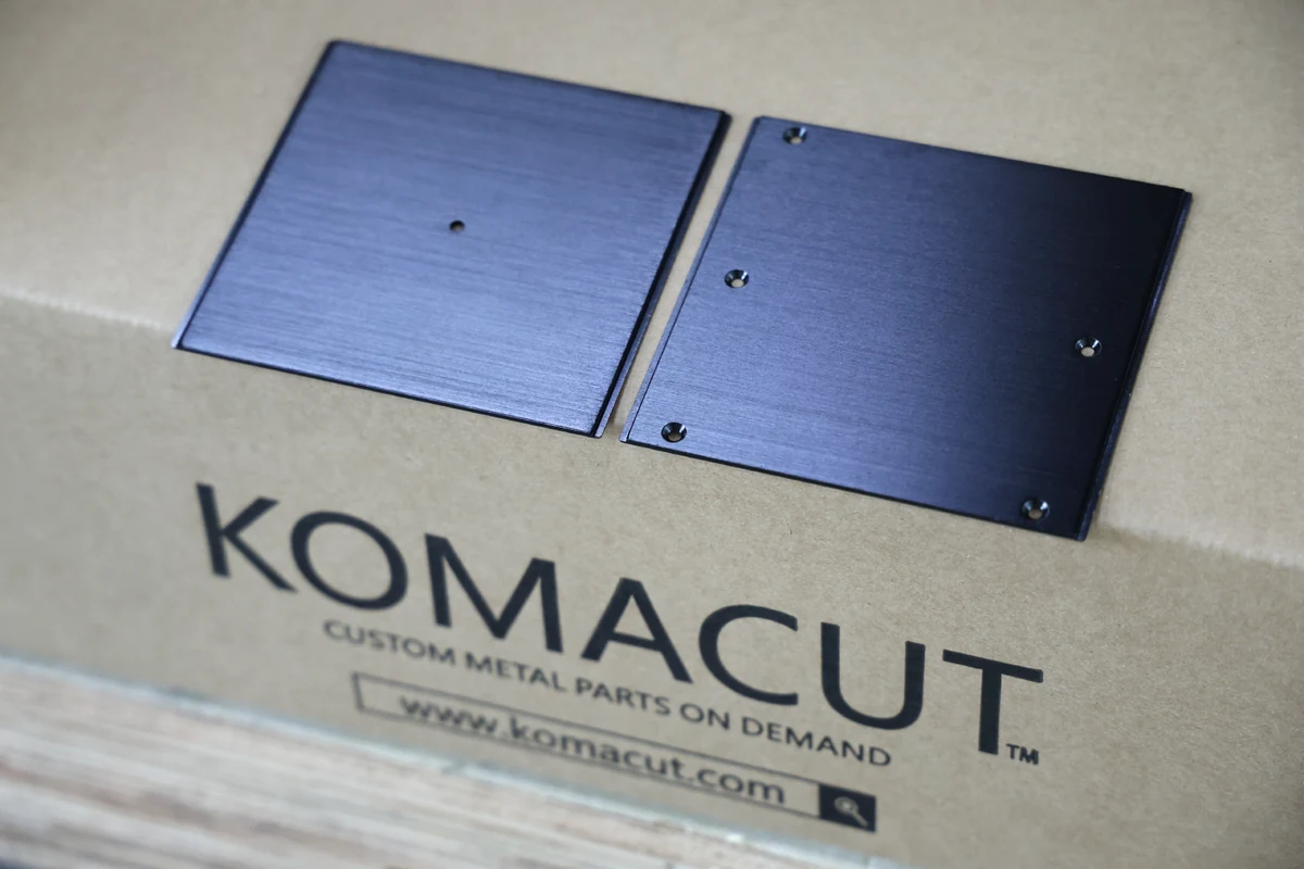 Black anodized aluminum sheet metal parts from Boda shown on a Boda shipping box