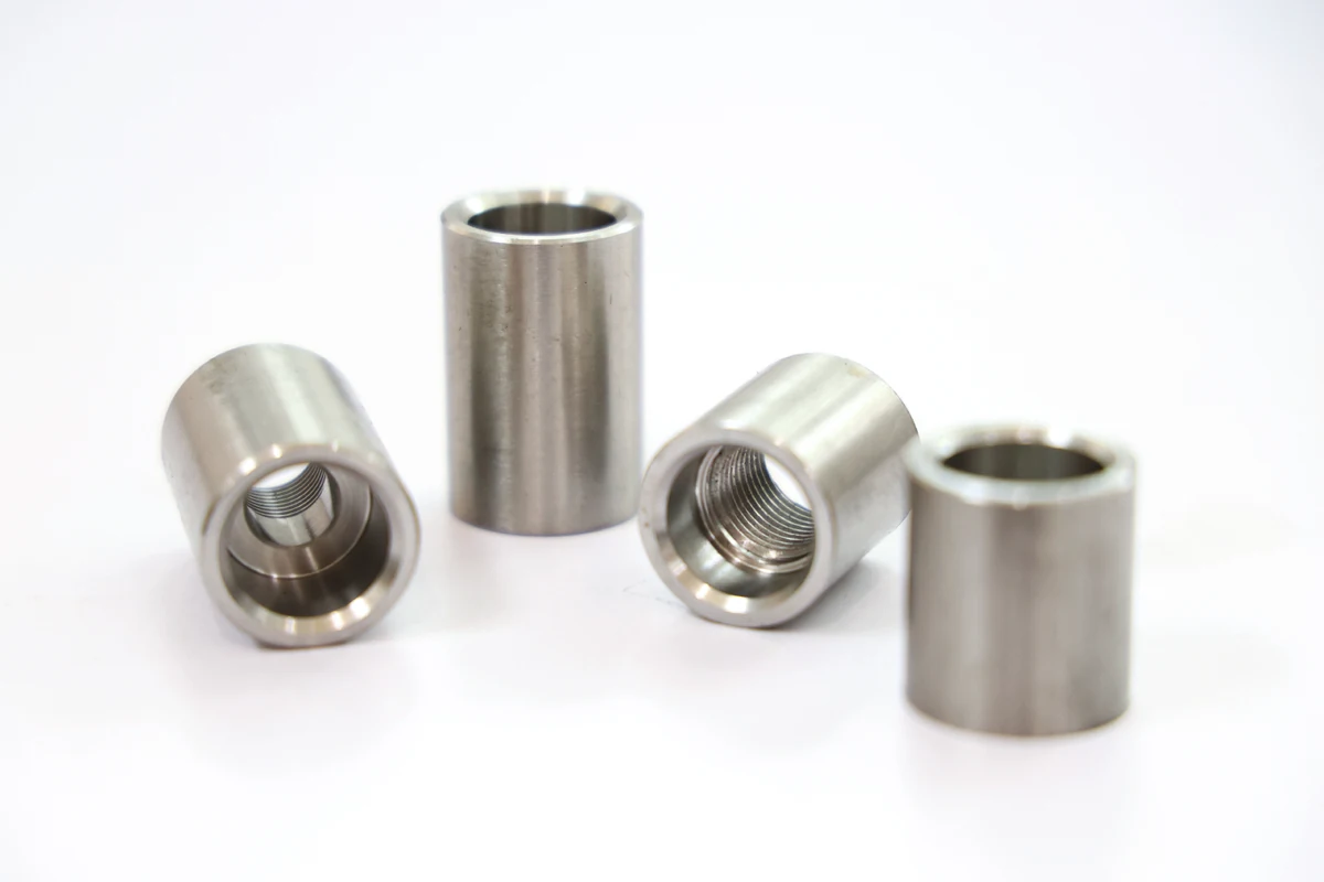 Four machined 304 stainless steel bushings, one internally threaded, on a white background